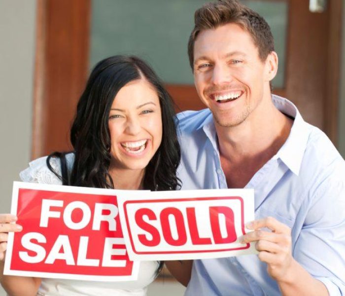 Happy couple holding for sale and sold signs